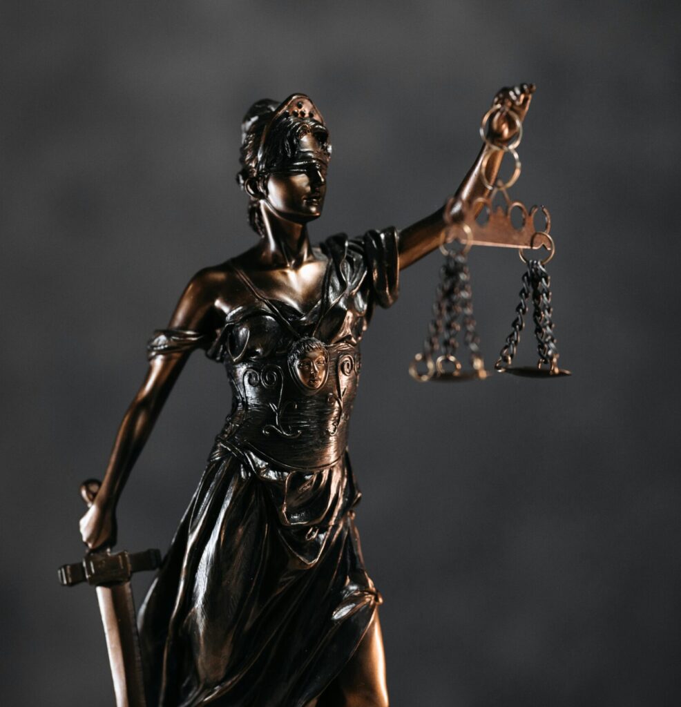 Detailed bronze Lady Justice statue with scales and sword against a dark background, symbolizing law and justice.